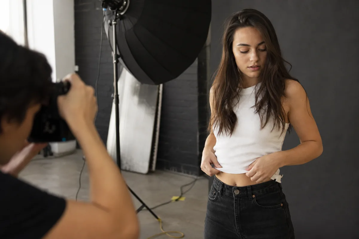 Modelo principiante entre pose y pose mientras el fotógrafo dispara en primer término