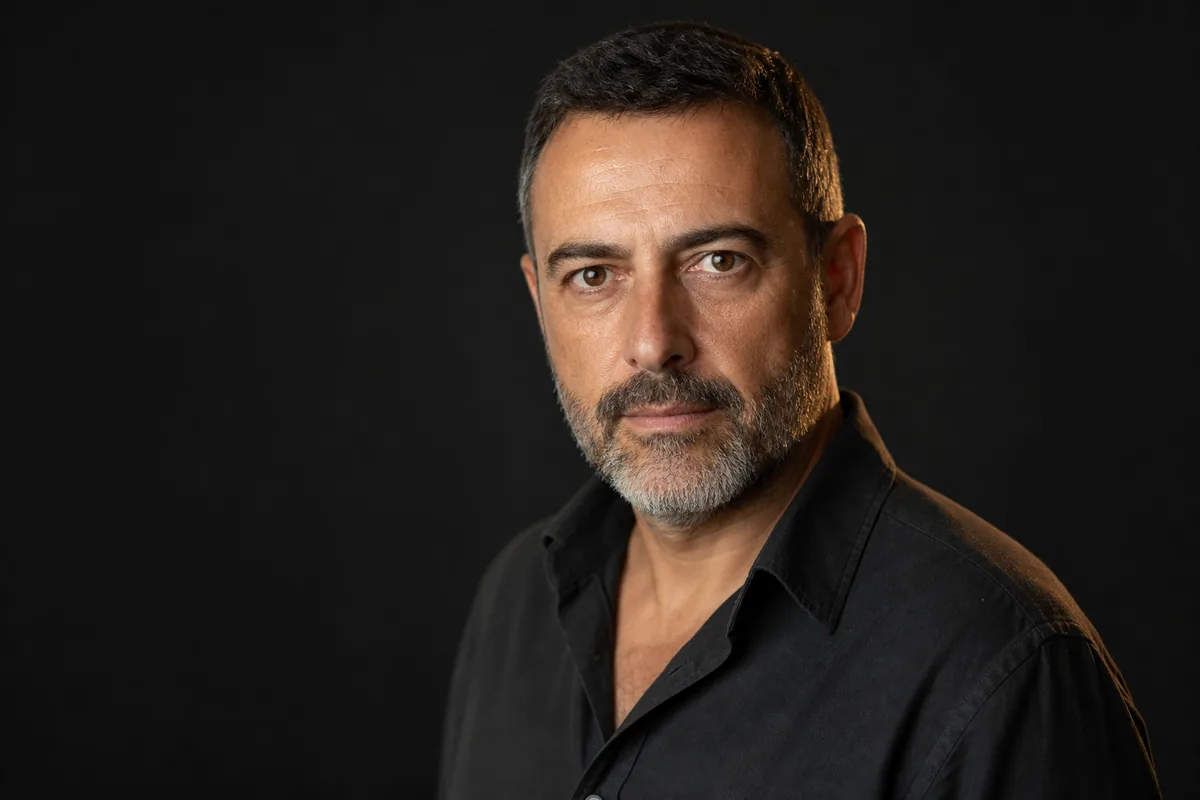 Headshot de actor de mediana edad con barba recortada, girado en tres cuartos