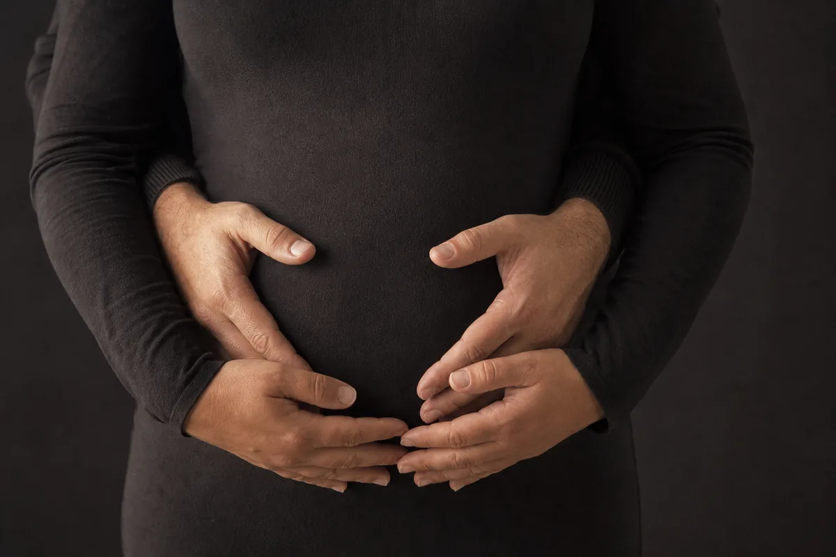 Dos pares de manos apoyadas sobre la tela del vestido a la altura del vientre